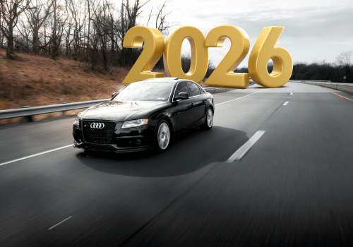 A sleek black car drives down an empty highway with bold 3D numbers "2026" hovering in the sky. The scene is dynamic and futuristic.